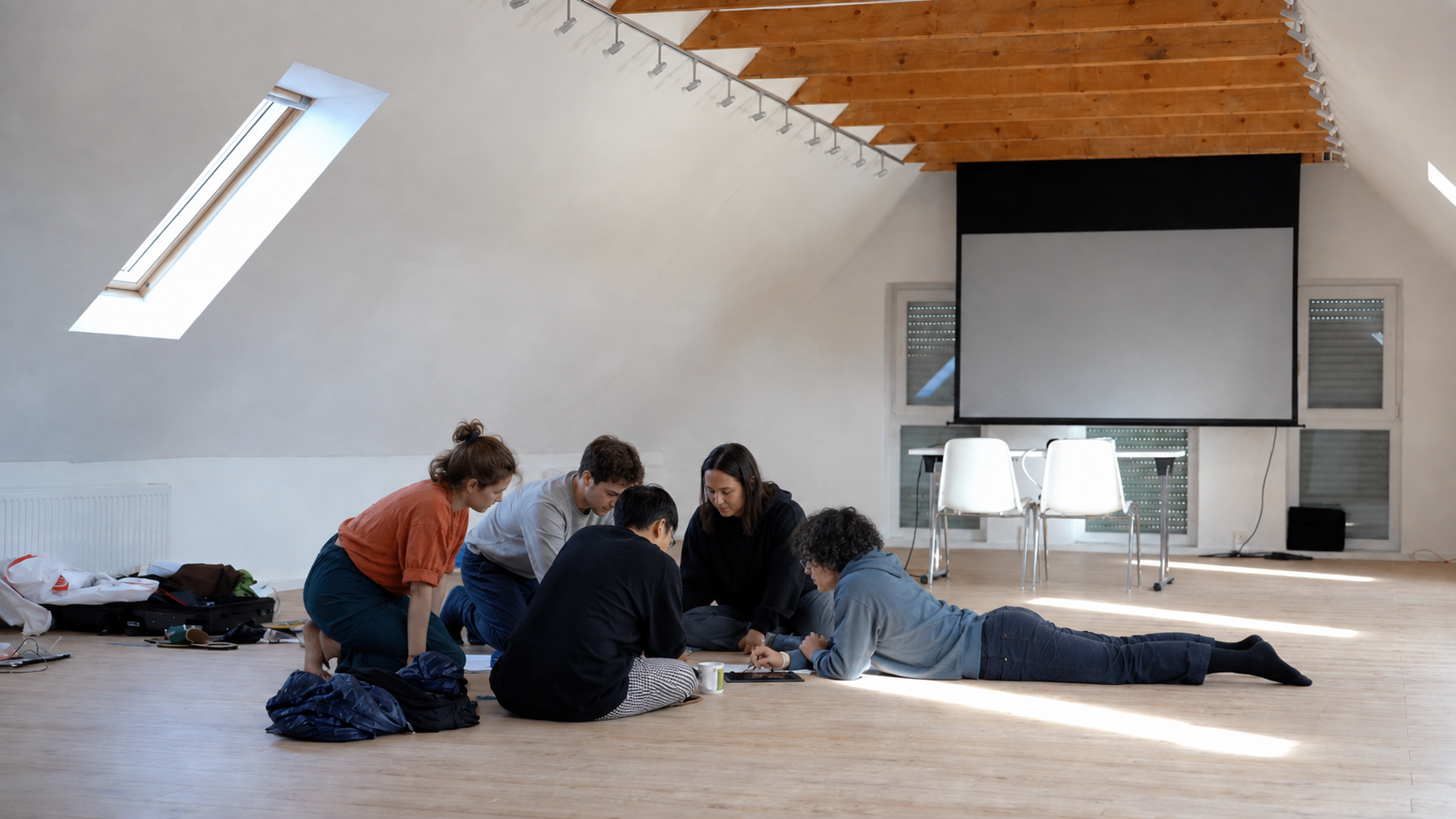 Gruppe arbeitet gemeinsam auf dem Holzboden im hellen Dachraum mit Leinwand